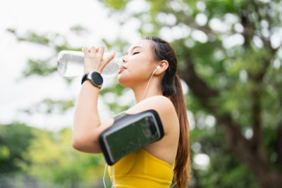 Asian young athlete after jogging in a park, relaxing and sipping water from a reusable water bottle. Taking a sip of water. preserving fluids. fitness objective. health and well-being. regimen for fitness and health. a lifestyle of healthfulness