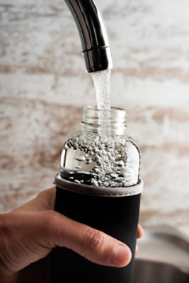 Refilling glass sports bottle with water from kitchen tap; reusable water bottle with water from a tap of a filtered water station or a domestic kitchen; water filtration, drinking water, sports bottle