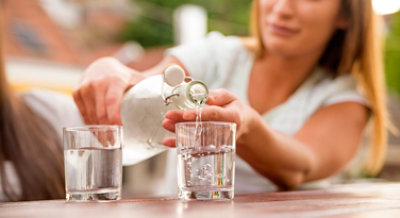 women pouring water from bottle jug into a glass